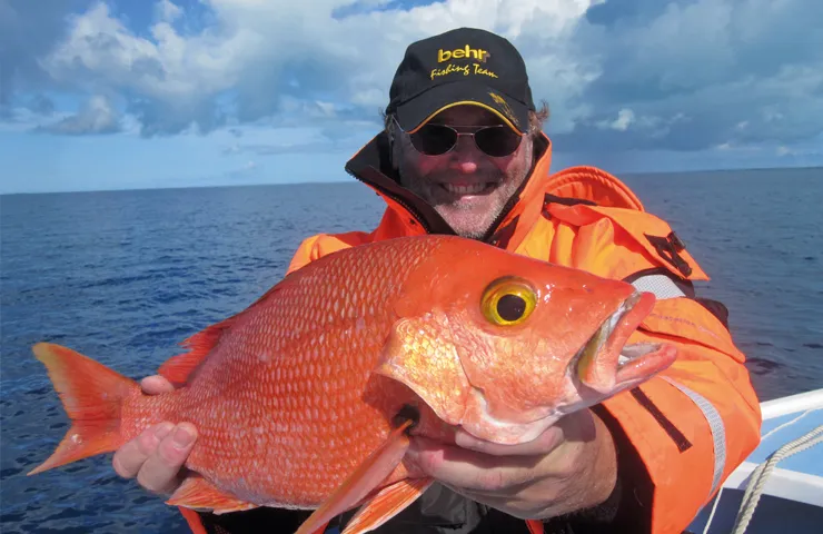 Angler auf dem Meer hält einen orangen Fisch in den Händen.